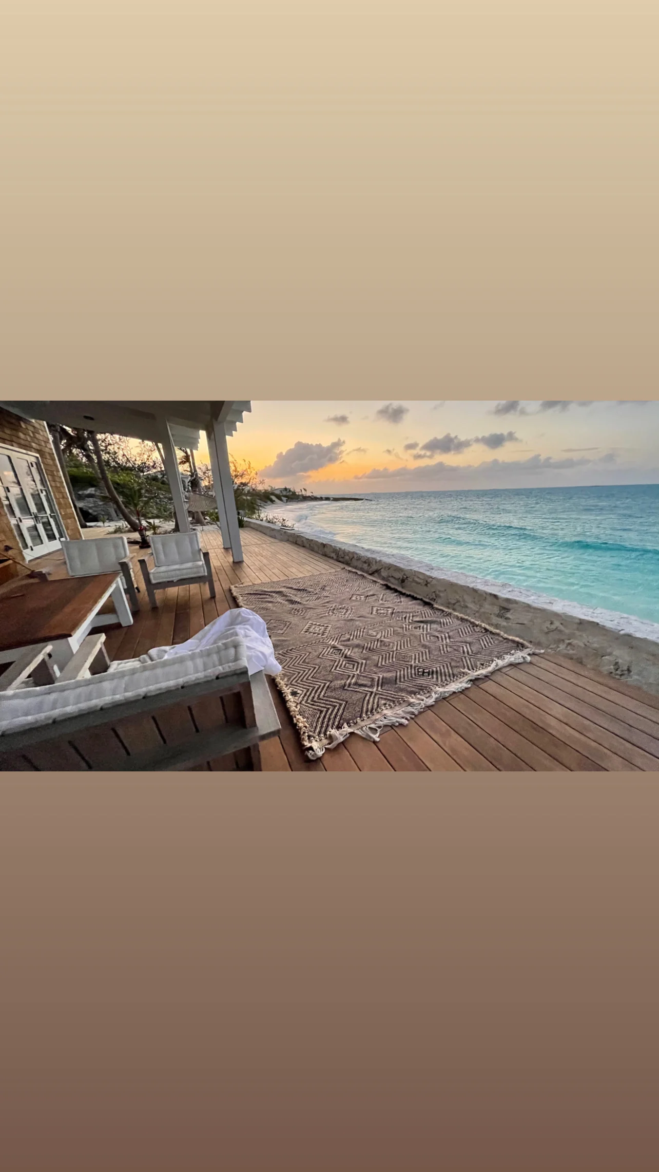 Wood deck with chairs and rug overlooking emerald water at sunset